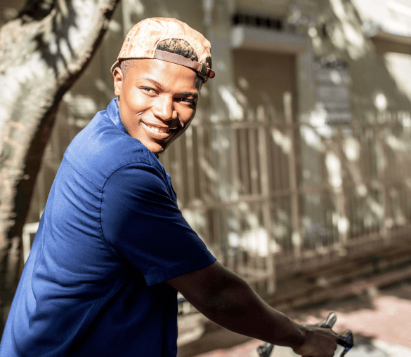 A young male with a cap worn backwards riding bike and looking over his shoulder